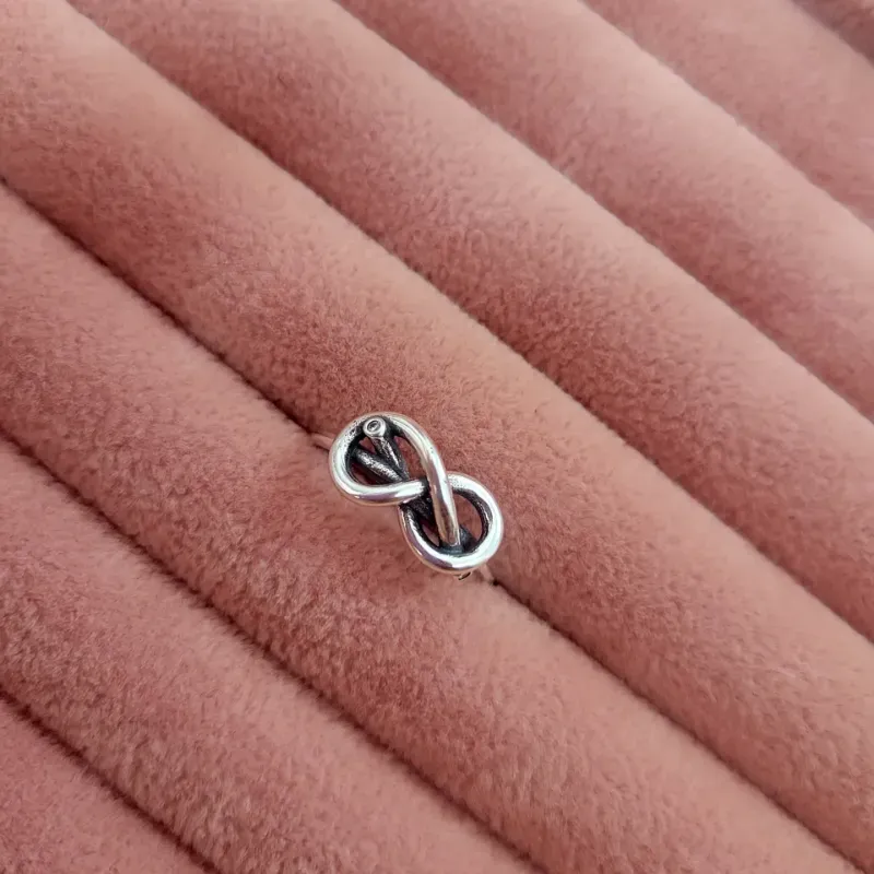 Anillo de infinito con pequeña piedra oscura incrustada.